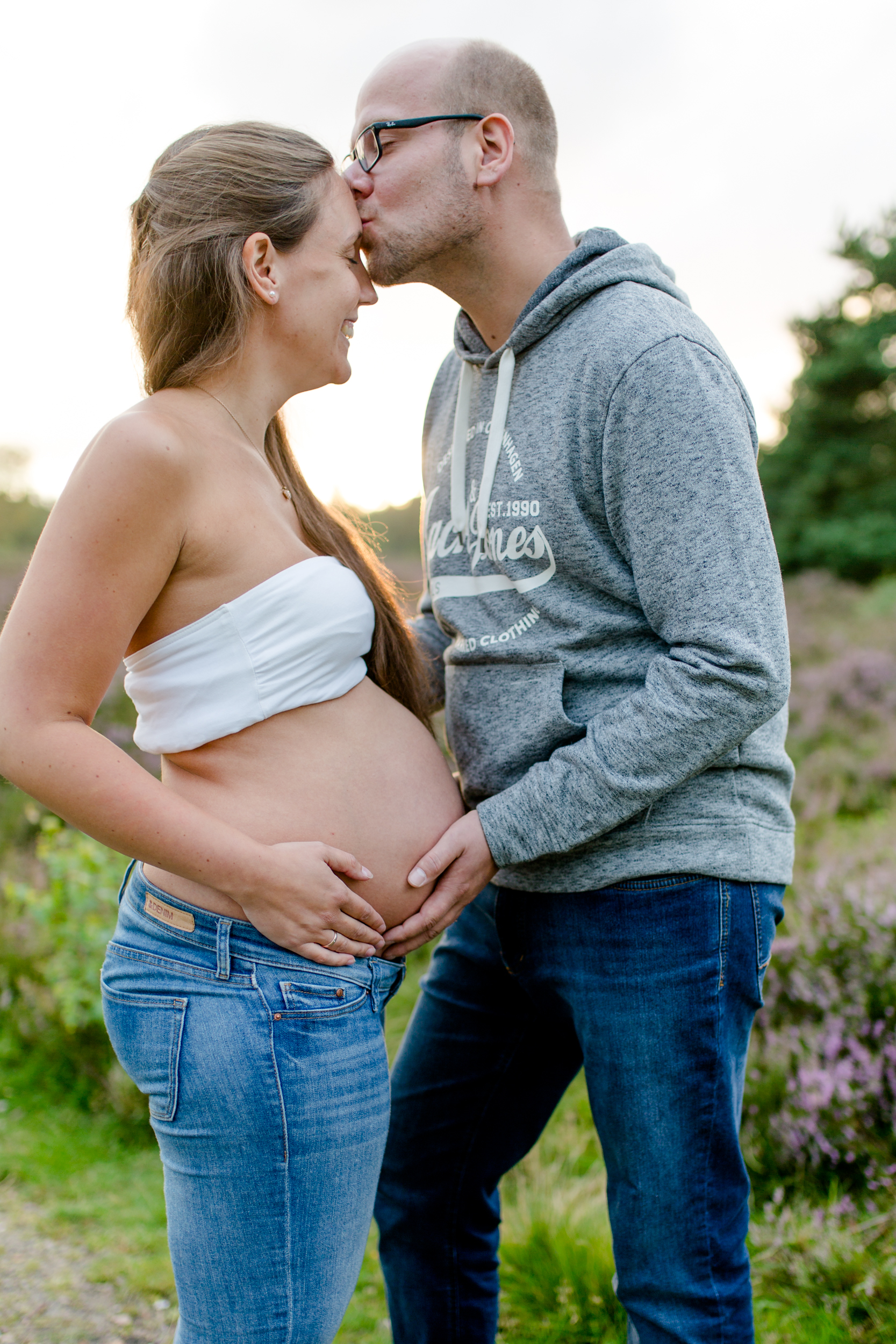 Babybauch-Shooting: Zärtlicher Moment, werdender Vater gibt seiner Partnerin einen Kuss auf die Stirn