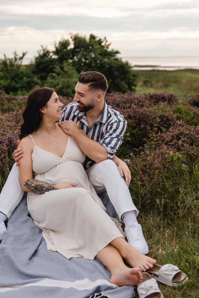 Babybauchfotografie in der Heide: Paar kuschelt auf Decke, zärtliche Liebkosung